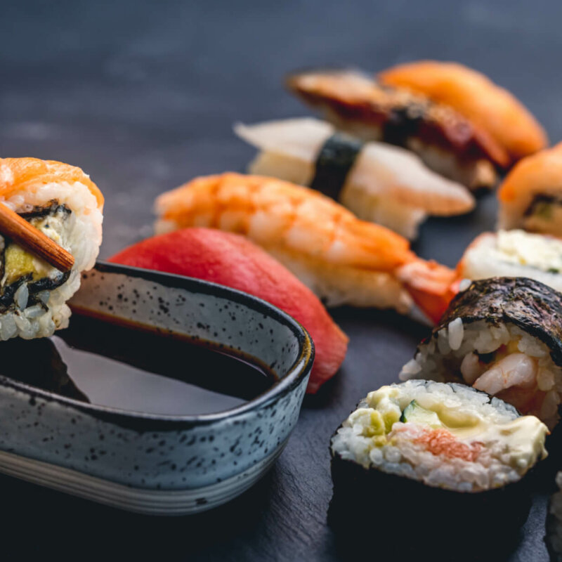 Person hold sushi maki roll with chopstick and put it to soy sauce. Oriental japanese healthy cuisine with rice and raw fish